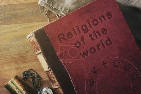 Detalle del viejo libro del estudio de las religiones en el mundo con texto grabado y símbolos de varias religiones sobre mesa de madera con objetos decorativos. Vista superior.