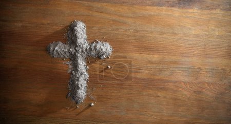 Cruz cristiana hecha con cenizas benditas sobre mesa de madera. Vista superior.