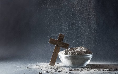 Ashes falling on Christian cross and container full of ashes isolated with dark gray background. Front view.