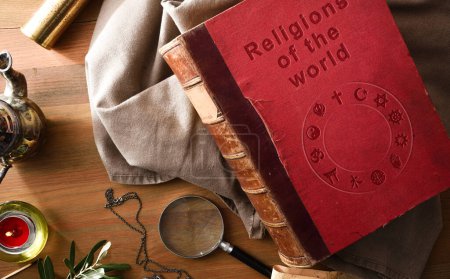 Altes und heruntergekommenes Buch über die Religionen der Welt mit eingravierten Buchstaben auf dem Einband und antiken Studien- und Abenteuerobjekten auf dem Holztisch. Ansicht von oben.