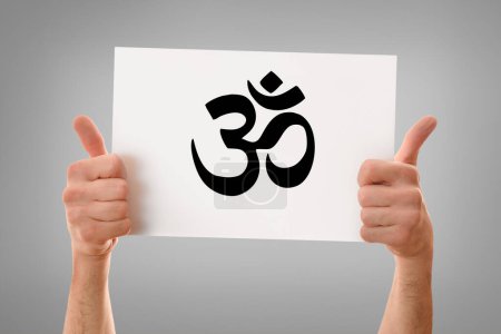 Hands of a religious man with okay sign holding a white poster with drawn hindu symbol with gray isolated background