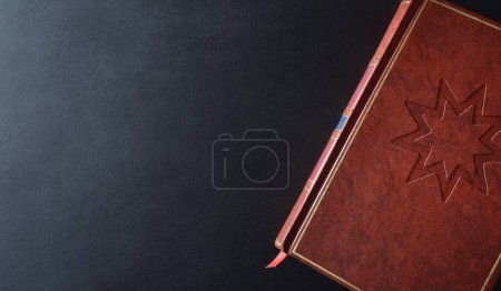 Bahai Kultur und Religion Buch mit religiösem Symbol eingraviert auf dem braunen Ledereinband auf einem schwarzen Tisch. Ansicht von oben.