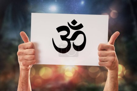 Hands of a religious man with okay sign holding a white poster with drawn hindu symbol with nature background