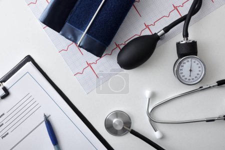 Comprobación de la salud del corazón y la presión arterial con herramientas de medición en la mesa del médico blanco con carpeta y electrocardiograma. Vista superior.