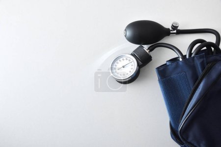 Detalle del monitor manual de presión arterial con manguito azul aislado en mesa blanca. Vista superior.