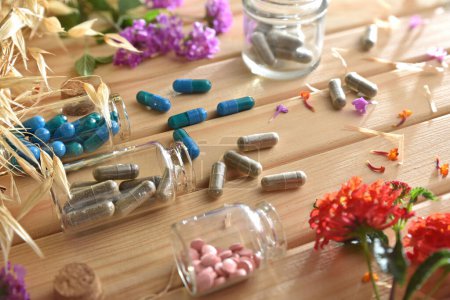 Natural medicines with plants and flowers on wooden table with capsules and pills in glass jars. Elevated view.