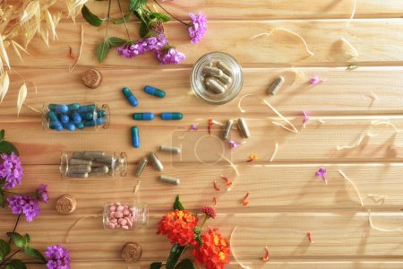 Natürliche Arzneimittel mit Pflanzen und Blumen auf Holztisch mit Kapseln und Pillen in Glasgefäßen. Ansicht von oben.