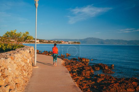 Téléchargez les photos : Coureur sur la plage du port de Malinska et vue panoramique sur le front de mer turquoise, île de Krk en Croatie - en image libre de droit