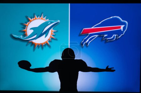 Photo for BUFFALO, USA, JANUARY 10, 2023: Miami Dolphins vs. Buffalo Bills. NFL Wild Card Round 2023, Silhouette of NFL player of american football. holding ball in hand. Big screen in background - Royalty Free Image