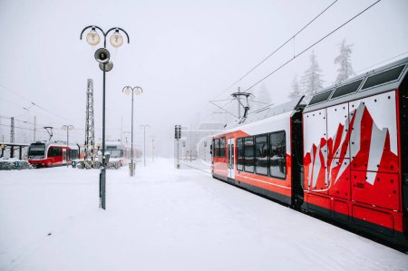 Photo for A crimson train stands at rest on a snowy station nestled in the heart of the majestic High Tatras. The red engine contrasts against the white winter wonderland, creating a striking image. - Royalty Free Image