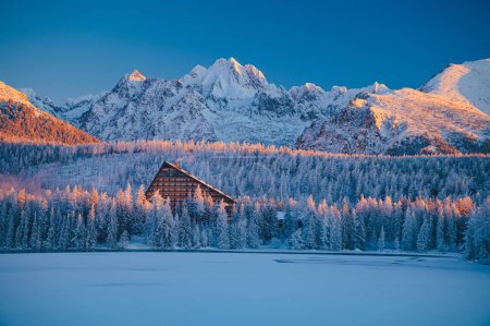 Téléchargez les photos : A winter's morning at Strbske Pleso, with the High Tatras standing tall and the lake reflecting the sun's first rays - en image libre de droit