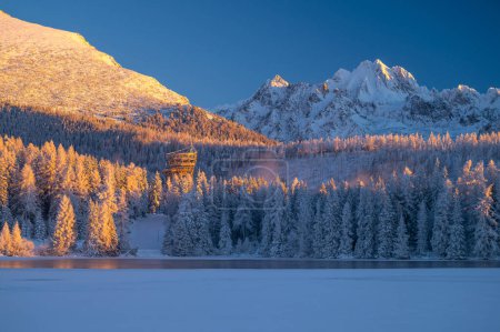 Téléchargez les photos : A winter's morning at Strbske Pleso, with the High Tatras standing tall and the lake reflecting the sun's first rays. - en image libre de droit