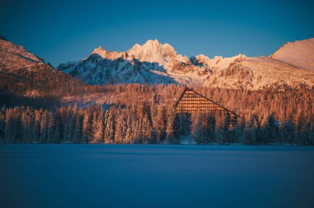Téléchargez les photos : Strbske pleso lake under the High Tatras, blanketed in snow and bathed in the warm light of a winter sunrise. - en image libre de droit