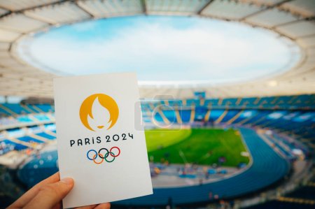 Photo for PARIS, FRANCE, JULY 7, 2023: Icon of Summer olympic Games Paris 2024 Held by Athlete. Modern Olympic Stadium in background. Wallpaper for Summer Olympic Game in Paris 2024. - Royalty Free Image