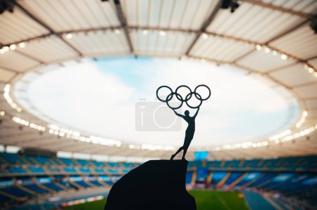 Téléchargez les photos : PARIS, FRANCE, 7 JUILLET 2023 : L'harmonie de l'athlétisme : la statue de l'athlète embrasse le cercle olympique contre le stade olympique moderne. Une photo de sport pour les Jeux Olympiques d'été de Paris 2024. - en image libre de droit