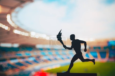 Foto de Igniting the Spirit: Silhouette of Male Athlete Carying the Torch Relay (en inglés). Modern Track and Field Stadium as the Striking background (en inglés). Capturando la esencia de los Juegos de Verano 2024 en París - Imagen libre de derechos