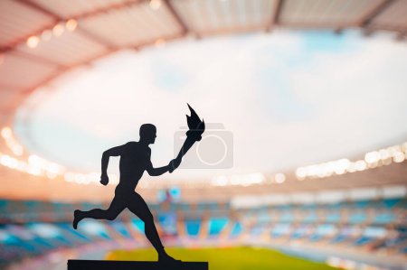 Photo for Igniting the Spirit: Silhouette of Male Athlete Carrying the Torch Relay. Modern Track and Field Stadium as the Striking Backdrop. Capturing the Essence of Summer Games 2024 in Paris - Royalty Free Image