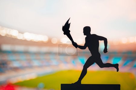 Téléchargez les photos : Symbole de l'unité : silhouette de l'athlète portant le relais de la flamme contre le stade moderne d'athlétisme. Une photo captivante pour le match d'été 2024 à Paris - en image libre de droit
