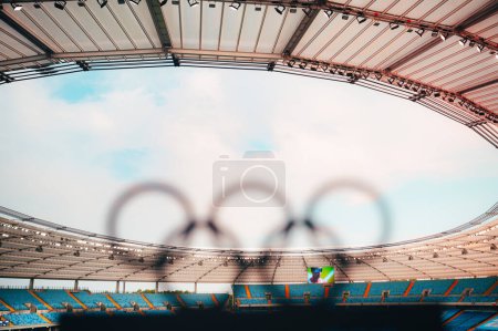 Foto de PARÍS, FRANCIA, 7 DE JULIO DE 2023: Silueta de anillos olímpicos abrazando un estadio olímpico moderno en el fondo - Imagen libre de derechos