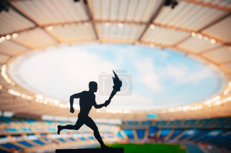Foto de Silueta del atleta masculino que lleva el relevo de la antorcha, iluminando la pista moderna y el estadio de campo. Una cautivadora instantánea para el juego de verano 2024 en París. - Imagen libre de derechos