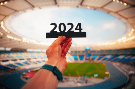 Photo for Silhouette of '2024' Holding in hand by Athlete. Sign Signals the Start of Sports Year, Leading to Summer Games in Paris. Modern Sport Stadium in background - Royalty Free Image