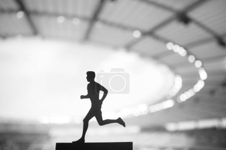 Foto de Silueta de un atleta masculino, un corredor dedicado, mostrando tenacidad en medio del sereno resplandor vespertino de un estadio deportivo moderno - Imagen libre de derechos