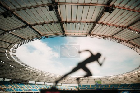 Téléchargez les photos : Libérer la vitesse : la silhouette d'un athlète, prêt et concentré, embrassant la lueur du crépuscule dans un stade sportif moderne. - en image libre de droit