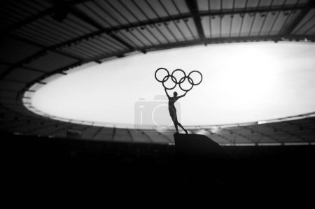 Foto de PARÍS, FRANCIA, 7 DE JULIO DE 2023: Poder simbólico: Estatua de la mujer atlética eleva el círculo olímpico en el estadio olímpico moderno. Foto deportiva para los Juegos Olímpicos de París 2024. - Imagen libre de derechos