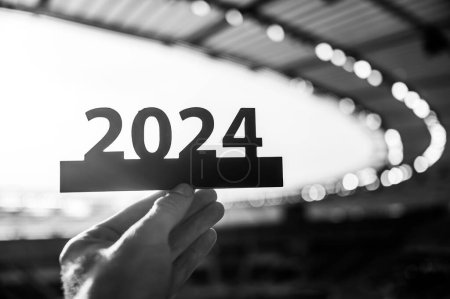 Foto de Silueta de '2024' Sosteniendo en la mano por Atleta. Sign señala el inicio del año deportivo, que conduce a los juegos de verano en París. Estadio deportivo moderno en segundo plano - Imagen libre de derechos