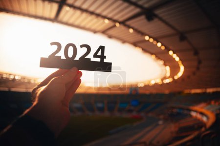 Téléchargez les photos : Silhouette de '2024' Tenue en main par l'athlète. Signalisation du début de l'année sportive, menant aux Jeux d'été à Paris. Stade de sport moderne en arrière-plan - en image libre de droit