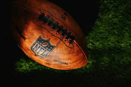 Téléchargez les photos : NEW YORK, États-Unis, 11 SEPTEMBRE 2023 : Vue détaillée de la boule en cuir de la NFL sur le terrain vert, couverte de lumière du soir et d'ombre. Photo illustrative, espace de montage noir - en image libre de droit