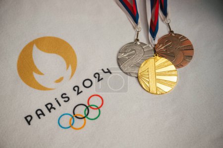 Photo for PARIS, FRANCE, JANUARY 4. 2024: Dazzling Arrangement: Gold, Silver, and Bronze Medals Resting on a White Blanket with Paris 2024 Olympics Logo - Royalty Free Image
