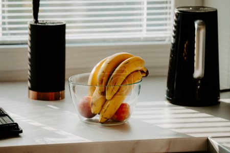 Foto de Un plátano descansa en un recipiente de vidrio en el mostrador de la cocina, bañado en el agradable resplandor de la luz del sol brillante - Imagen libre de derechos
