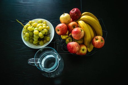 Foto de Plátano, manzana y uvas en una mesa de cocina oscura - Imagen libre de derechos