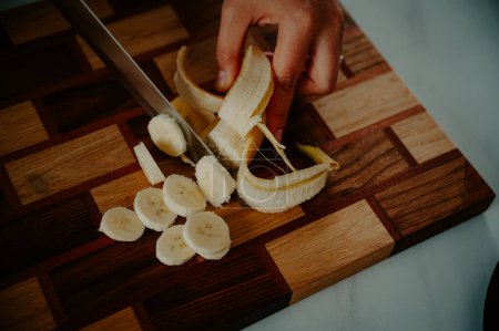Una mujer corta un plátano en trozos pequeños y toma un desayuno nutritivo fresco y saludable lleno de vitaminas