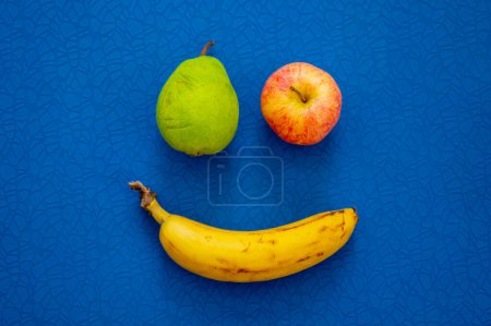 Foto de Sonríe desde frutas plátano, manzana y pera. Estera azul en el fondo - Imagen libre de derechos