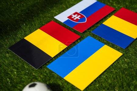 Groupe E au tournoi de football européen en Allemagne en 2024. Drapeaux de Belgique, Slovaquie, Roumanie, Ukraine et ballon de football sur herbe verte
