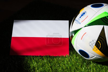 Photo for MUNICH, GERMANY, APRIL 17, 2024: Poland national flag and official soccer ball of Euro 2024 football tournament in Germany placed on green grass. Black background, edit space - Royalty Free Image