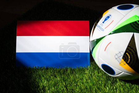 Téléchargez les photos : HAMBURG, ALLEMAGNE, 17 AVRIL 2024 : Drapeau national néerlandais et ballon de football officiel du tournoi de football Euro 2024 en Allemagne placé sur l'herbe verte. Arrière-plan noir, modifier l'espace - en image libre de droit