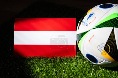 Foto de LEIPZIG, ALEMANIA, 17 DE ABRIL DE 2024: Bandera nacional de Austria y balón de fútbol oficial del torneo de fútbol Euro 2024 en Alemania colocado sobre hierba verde. Fondo negro, editar espacio - Imagen libre de derechos