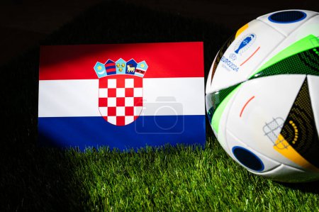 Photo for MUNICH, GERMANY, APRIL 17, 2024: Croatia national flag and official soccer ball of Euro 2024 football tournament in Germany placed on green grass. Black background, edit space - Royalty Free Image