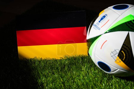 Foto de HAMBURG, ALEMANIA, 17 DE ABRIL DE 2024: Bandera nacional de Alemania y balón de fútbol oficial del torneo de fútbol Euro 2024 en Alemania colocado sobre hierba verde. Fondo negro, editar espacio - Imagen libre de derechos