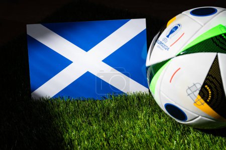 Photo for HAMBURG, GERMANY, APRIL 17, 2024: Scotland national flag and official soccer ball of Euro 2024 football tournament in Germany placed on green grass. Black background, edit space - Royalty Free Image