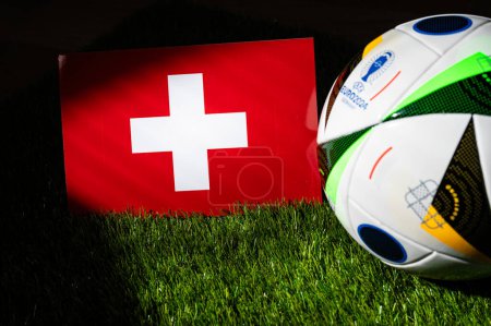 Foto de MUNICH, ALEMANIA, 17 DE ABRIL DE 2024: Bandera nacional de Suiza y balón de fútbol oficial del torneo de fútbol Euro 2024 en Alemania colocado sobre hierba verde. Fondo negro, editar espacio - Imagen libre de derechos