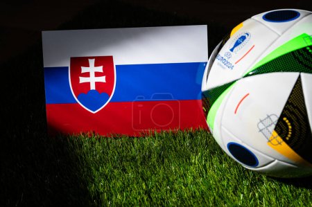 Photo for BERLIN, GERMANY, APRIL 17, 2024: Slovakia national flag and official soccer ball of Euro 2024 football tournament in Germany placed on green grass. Black background, edit space - Royalty Free Image