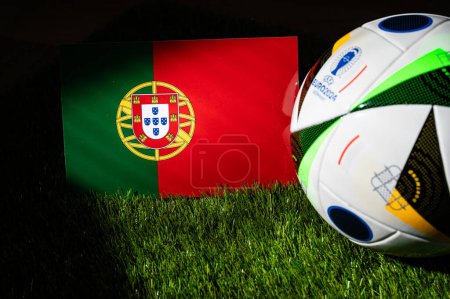 Foto de LEIPZIG, ALEMANIA, 17 DE ABRIL DE 2024: Bandera nacional de Portugal y balón de fútbol oficial del torneo de fútbol Euro 2024 en Alemania colocado sobre hierba verde. Fondo negro, editar espacio - Imagen libre de derechos