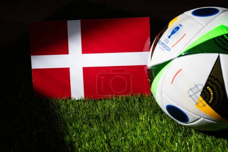 Téléchargez les photos : LEIPZIG, ALLEMAGNE, 17 AVRIL 2024 : Drapeau national danois et ballon de football officiel du tournoi de football Euro 2024 en Allemagne placé sur l'herbe verte. Arrière-plan noir, modifier l'espace - en image libre de droit