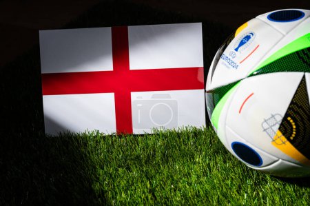Photo for BERLIN, GERMANY, APRIL 17, 2024: England national flag and official soccer ball of Euro 2024 football tournament in Germany placed on green grass. Black background, edit space - Royalty Free Image