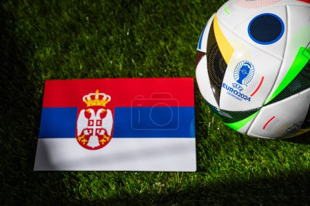 Téléchargez les photos : LEIPZIG, ALLEMAGNE, 17 AVRIL 2024 : Drapeau national de Serbie et ballon de football officiel du tournoi Euro 2024 en Allemagne placé sur l'herbe verte. Arrière-plan noir, modifier l'espace - en image libre de droit