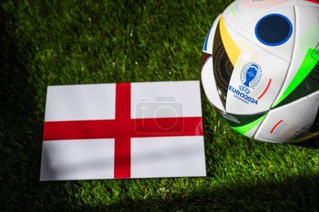 Photo for BERLIN, GERMANY, APRIL 17, 2024: England national flag and official soccer ball of Euro 2024 football tournament in Germany placed on green grass. Black background, edit space - Royalty Free Image